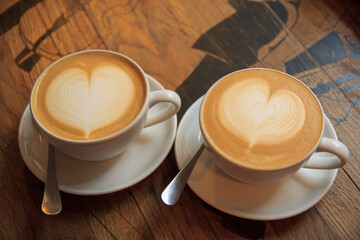 Two cups of cappuccino with latte art on wooden table. Beautiful foam, white ceramic cups. cups of coffee on wooden background with both heart shaped latte art on top. Morning breakfast.