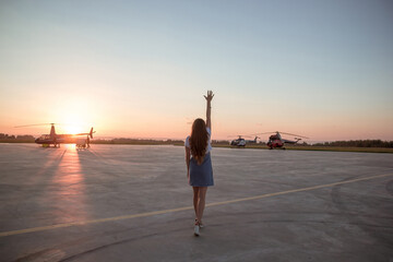 woman with raised hand standing on the airfield. Sunset soft light. Magestic landscape.  a young girl with long hair on the background of helicopters