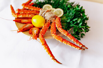 Shrimp, crab, lemon and greens on a plate on a white background.