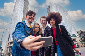 Group of four multiethnic young tourist friends outdoor using smartphone taking selfie
