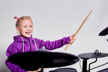 Happy caucasian kid girl drummer. Girl playing on elettronic drum kit or learns to play drums in music school. Emotional portrait. Mock up, studio on gray background. Free space for advertisement.