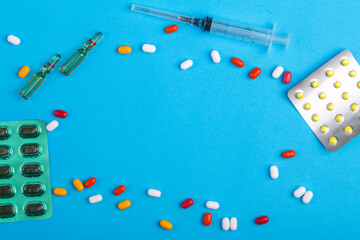 Scattered pills and medicines in blisters on a blue background and syringe copy place.