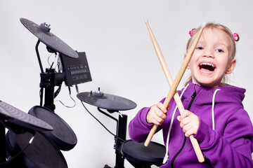 Happy caucasian kid girl drummer. Girl playing on elettronic drum kit or learns to play drums in...