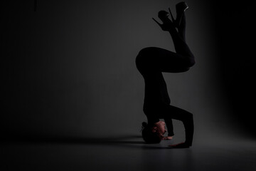 Plakat long-legged girl dancer in a black bodysuit and stockings in a photo studio in unusual poses on a gray background