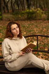 Obraz premium a young beautiful girl is sitting on a bench in an autumn Park, reading a book 