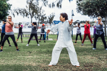 Mature chinese woman do tai chi with blirred group of people outdoor in the park - obrazy, fototapety, plakaty