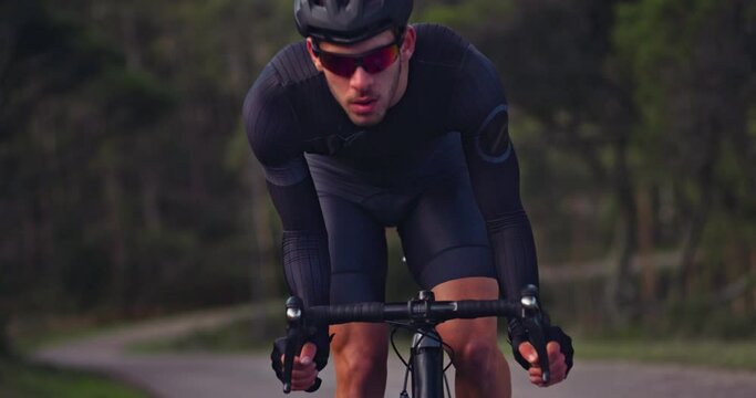 Close-up of professional cyclist riding bike uphill on a forest