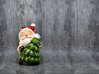 Statuette of Santa Claus with a Christmas tree on a gray background with space for text. Christmas...