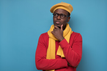 Young African American man in glasses looking up with thoughtful and skeptical expression, holding...