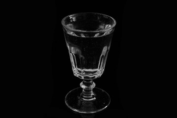 Closeup of a glass of water on a black background. Still life of an illuminated vintage glass on a black backdrop.