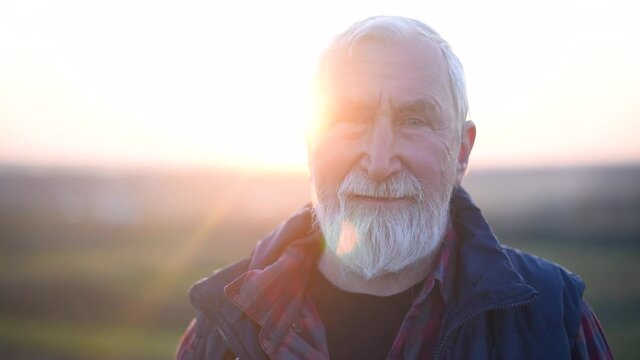 An elderly man with gray hair and beard in the plaid shirt on the background of the mountain at sunset
