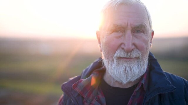 An elderly man with gray hair and beard in the plaid shirt on the background of the mountain at sunset