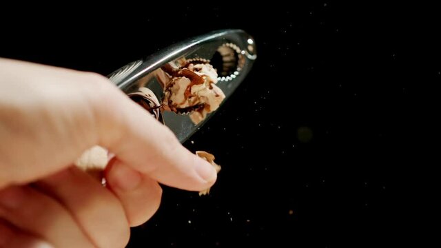 Male hand crushing a walnut with a steel nutcracker. Slow motion.