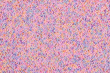 Fototapeta na wymiar Pastel color balls texture. Styrofoam or Polystyrene foam background. Mix of colorful sugar balls, used to decorate baking and sweets. Rainbow colored sugar chips or dragee spins, confectionery