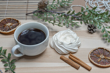 A mug of coffee on a wooden table, airy meringue, dried orange slice, cinnamon and winter holiday accessories. New year christmas card