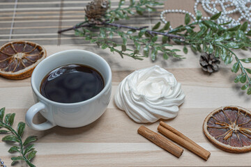 A mug of coffee on a wooden table, airy meringue, dried orange slice, cinnamon and winter holiday accessories. New year christmas card