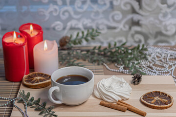 Christmas candles, a mug of coffee on a wooden table, airy meringue, dried orange slice, cinnamon and winter holiday accessories. New Year