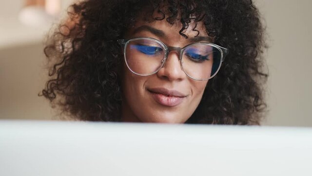 Young positive woman sitting indoors at home and using laptop computer while drinking coffee
