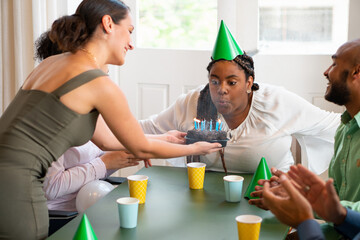 Happy business woman blowing candles in office or coworking space. Festive, anniversary, surprise, fun, celebration, party concept..