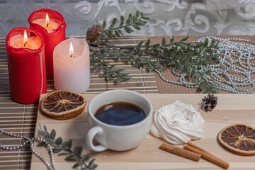 Christmas candles, a mug of coffee on a wooden table, airy meringue, dried orange slice, cinnamon and winter holiday accessories. New Year