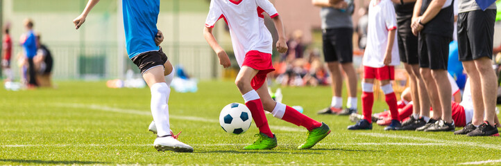 Kids in soccer running duel. Boys in two football teams running after classic soccer ball on school tournament. Horizontal sports background. Legs of young players on football pitch © matimix