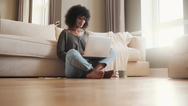 Young optimistic african woman sitting indoors at home and using laptop computer
