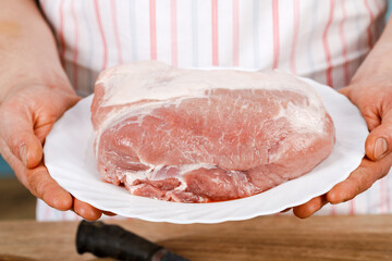 The cook shows fresh meat for cooking on a plate.