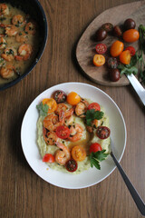 Glazed shrimp with garlic and honey sauce over creamy mashed potatoes and topped with colourful cherry tomatoes and coriander leaves. Beautiful spring meal plated on wooden table. 