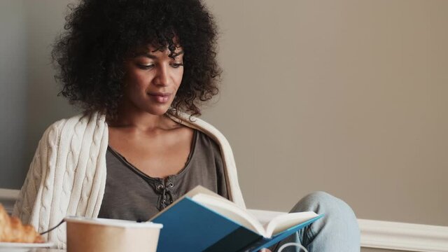 Positive african woman indoors at home reading a book