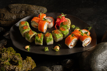 A set of several types of sushi on a beautiful black plate. Japanese dish. Sushi rolls made of salmon, shrimp, avocado, red caviar, rice, ginger, wasabi and peanut sauce.
