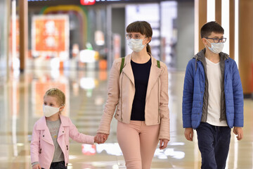 Young mother with her daughter and son in protective masks are walking along the mall