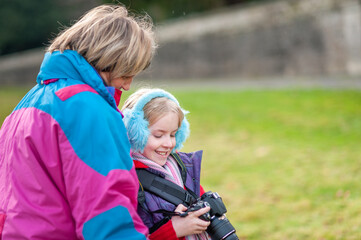 Happy young girl holding a camera and wearing blue ear muffs shows camera to mother