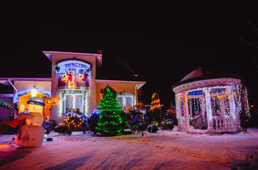 House Adorned with Christmas Holiday Lights and Decorations including Santa Snowman and Giant Trees Illuminated at Night.Christmas house