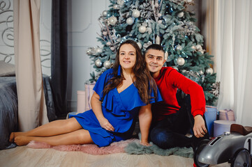 Young couple, man and woman posing under Christmas tree with gifts indoors. Christmas concept, gifts, memories of childhood.