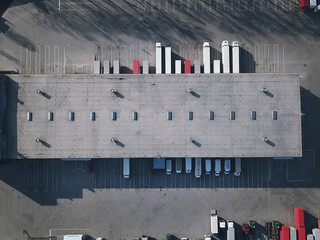 Aerial view of goods warehouse. Logistics center in industrial city zone from above. Aerial view of trucks loading at logistic center. View from drone.