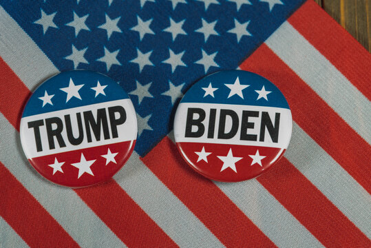 Washington DC--July 5, 2020; Round red white and blue Donald Trump and Joe Biden Presidential campaign buttons sit on an American flag on a wooden table.