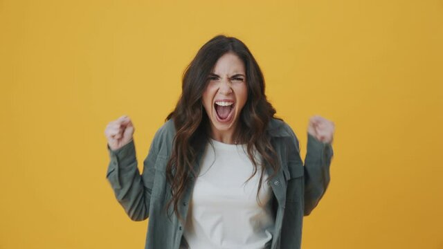 An angry woman is screaming while standing isolated over yellow background