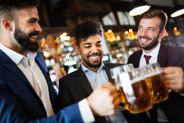 Cheerful old friends having fun and drinking beer at bar counter in pub.