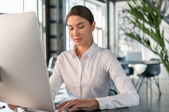 Female office manager in white shirt in office interior background, beautiful woman office worker looking at the keyboard. Woman working with computer in big office, concept of work