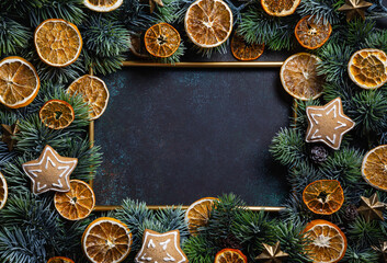 Christmas composition. Frame with gingerbread, pine branches and dried orange chips slices on green background.