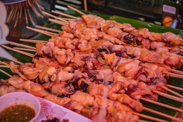 Close up raw squid meat skewer on banana leaf in the fresh market of thailand with spicy seafood sauce.Thailand street food