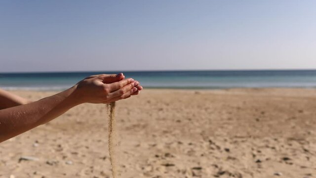 Pouring sand in woman's hand. Sand is falling through her fingers.Woman pours beach sand from her hands