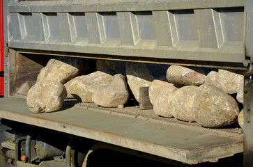 moving granite river boulders from the body of a truck. open sidewalls, stones are rolled on the...