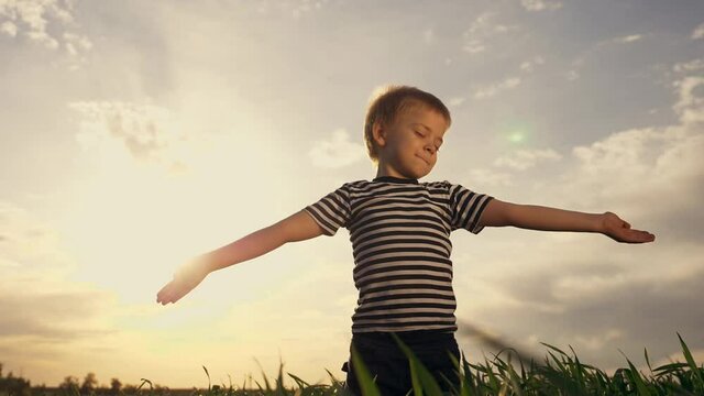 Happy kid praying in the park. Kid in a field with wheat praying raised his hands to the sides. Happy child closing his eyes looks to the sky. Child prays to the sky childhood dreams. Spiritual prayer