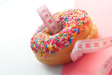 Close up of donuts and measurement tape on pink background.