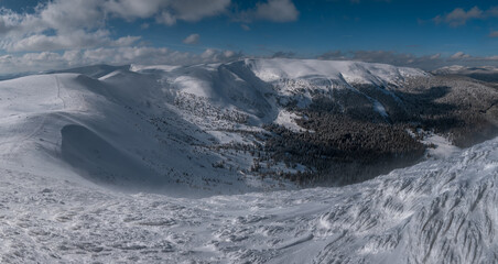 Snow and wind formed ice formations covered winter mountain plateau, tops with snow cornices in far. Magnificent sunny day on picturesque beautiful alpine ridge.