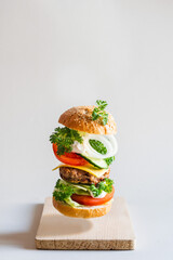 Delicious burger with flying ingredients on gray background, selective focus