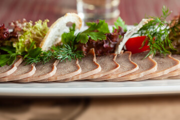 Delicious restaurant dish of thinly sliced boiled beef tongue with herbs on a large white plate with a selective focus.