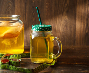 Kombucha tea in a glass Cup with a tube and a can of Kombucha, on a dark wooden background with a measuring tape