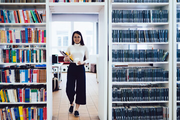 Smiling Asian woman with books and disposable cup of coffee in library